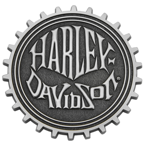A circular Harley-Davidson logo plaque or badge with a gear-like outer edge, shown on a plain white background.