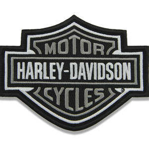 An embroidered Harley-Davidson patch in the brand's classic bar-and-shield style, featuring black, white, and gray colors on a plain white background.