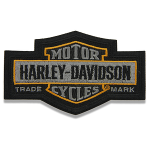 An embroidered Harley-Davidson patch featuring the classic bar and shield design in black, gray, and gold on a white background.
