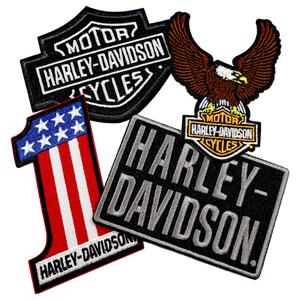 Four embroidered Harley-Davidson patches arranged on a plain white background, including a classic shield logo patch, an eagle patch, a black-and-white Harley-Davidson sign patch, and a red, white, and blue American flag patch.
