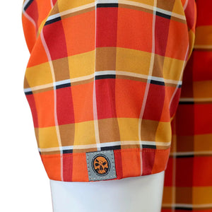 Close-up of a plaid shirt sleeve on a white mannequin torso, featuring orange, red, yellow, and brown stripes with a small circular skull patch near the cuff.