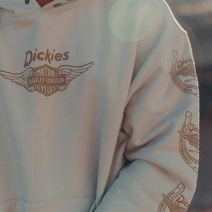 A close-up of a light beige hoodie featuring a brown 'Dickies' Harley-Davidson logo on the chest and matching logos printed down the sleeve.