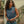 Woman wearing a sleeveless denim shirt with a logo, standing outdoors.