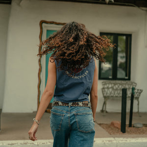 Person wearing a blue sleeveless shirt with text and jeans, standing in front of a building.