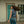Woman wearing a denim vest with a logo, standing in front of a building with a teal door.