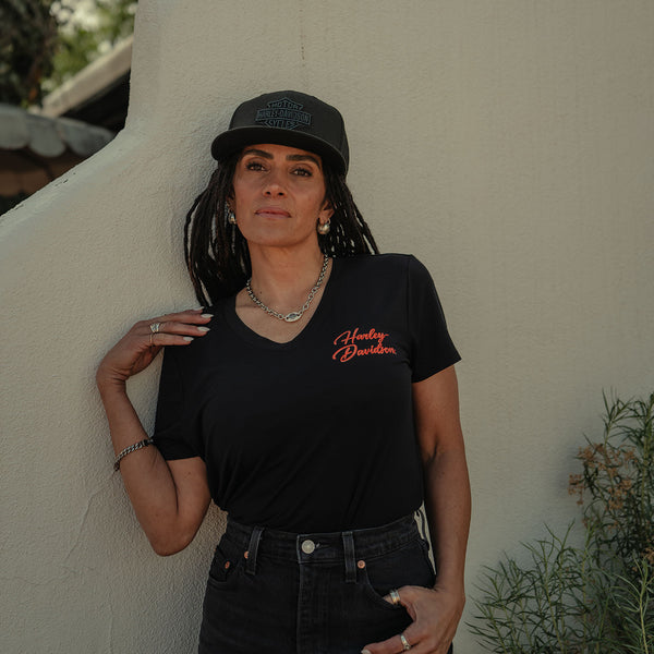 Person wearing a black Harley Davidson t-shirt and cap against a beige wall.
