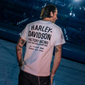 Person wearing a Harley-Davidson t-shirt with tattoos visible on arms, standing against a dark background.