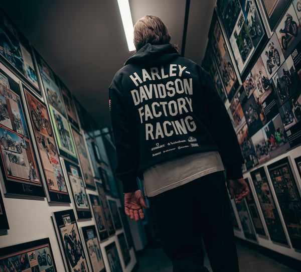 Person wearing a Harley Davidson Factory Racing jacket in a room with framed pictures on the wall.