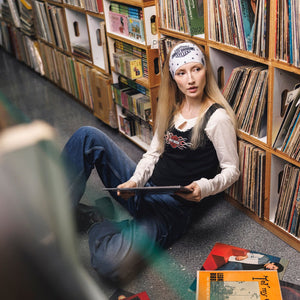 Person sitting on the floor surrounded by vinyl records and books in a library setting