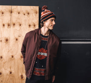 Man wearing a jacket and beanie with visible branding against a wooden panel background