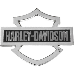 A Harley-Davidson shield emblem badge with a polished chrome silver border and a black center panel featuring the brand name in silver lettering.
