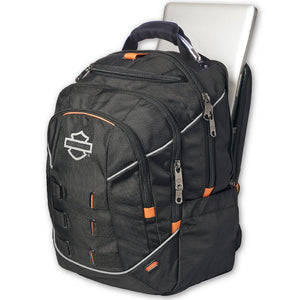 A black backpack with orange accents and a white Harley-Davidson logo on the front pocket, shown with a silver laptop partially inserted into a side pocket, against a plain white background.