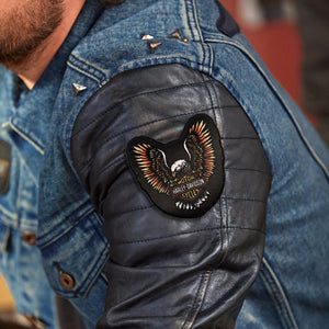 Close-up of a person wearing a blue denim jacket with a black leather sleeve patch featuring an eagle design and the text 'Harley-Davidson' and 'World Classic'.