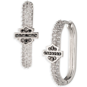 A pair of silver-toned huggie hoop earrings featuring a central shield-shaped motif set with dark gray stones and surrounded by rows of clear pavé stones, shown on a plain white background.