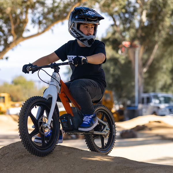 Child riding a balance bike with training wheels outdoors
