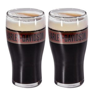 Two clear pint glasses filled with black beer and topped with white foam, each wrapped with a pink band printed with the Harley-Davidson logo, shown on a white background.