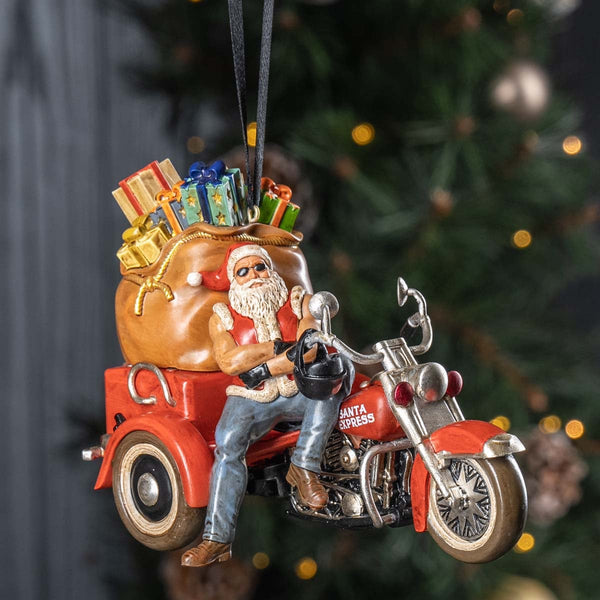 Decorative ornament of Santa Claus on a motorcycle with gifts, against a Christmas tree background.
