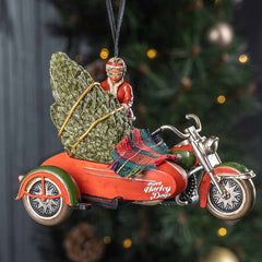 Decorative ornament of Santa Claus on a motorcycle with a Christmas tree, against a blurred Christmas tree background.