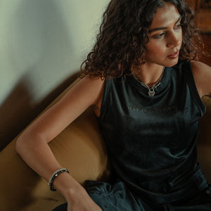 Woman sitting on a couch wearing a dark green dress with a necklace and bracelet.