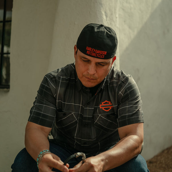 Man wearing a Harley Davidson cap and shirt, sitting against a white wall.