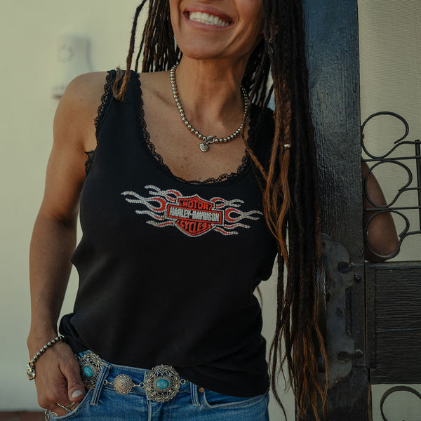 Woman wearing a black tank top with a Harley-Davidson flames blinged, standing